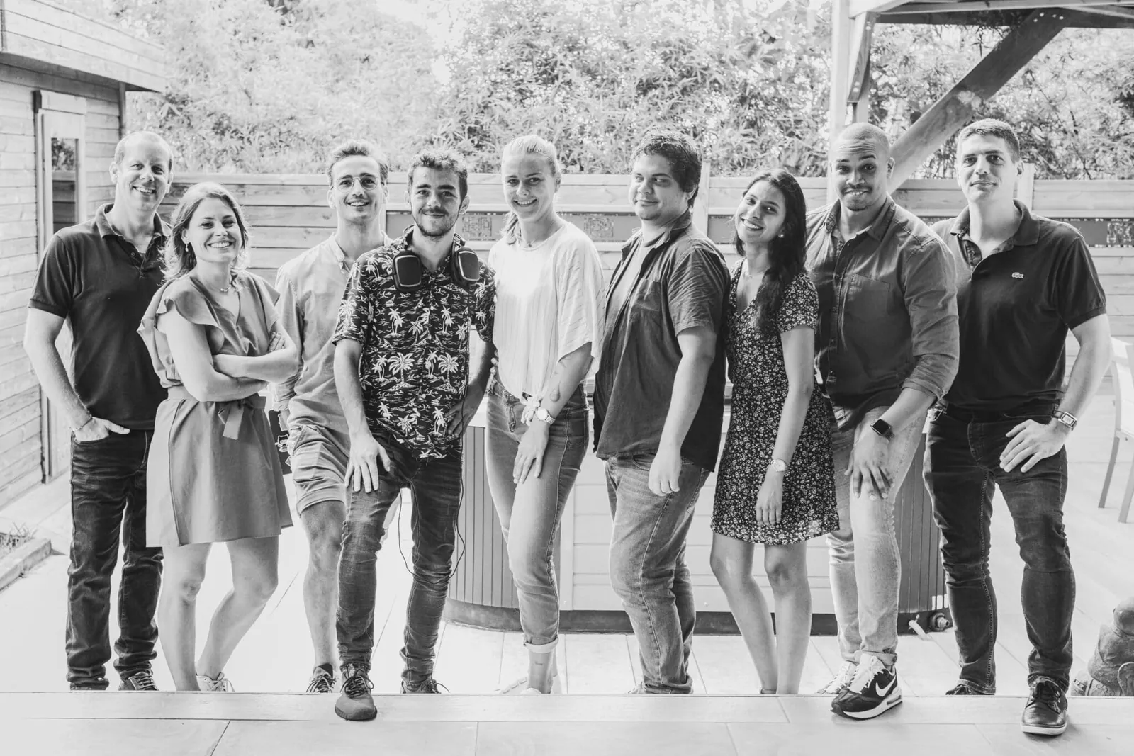 Photo de groupe en noir et blanc de neuf membres de l'équipe Squirrel, souriants, sur une terrasse en bois à La Réunion